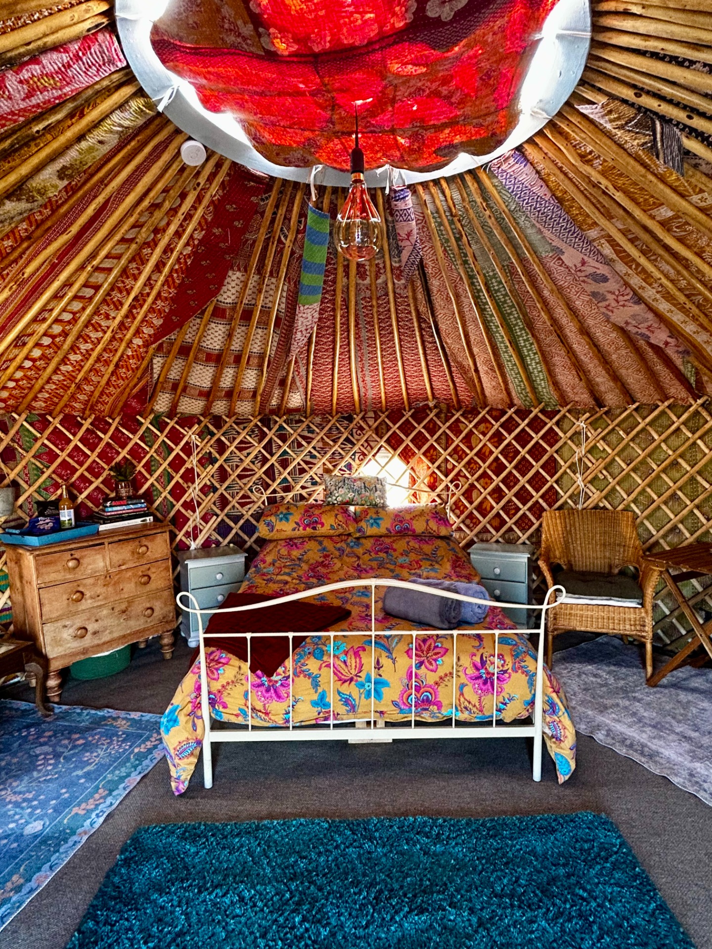 Cozy Yurt interior with colorful bedding, patterned rugs, and a hanging lantern under a red canopy.