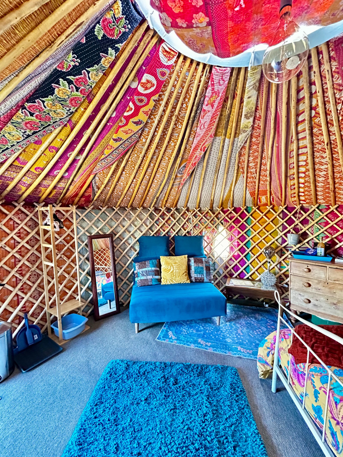 Colorful patterned fabric canopy and curtains fill a cozy room, with blue cushions, rug, and wooden dresser. Small double fold out sofa bed